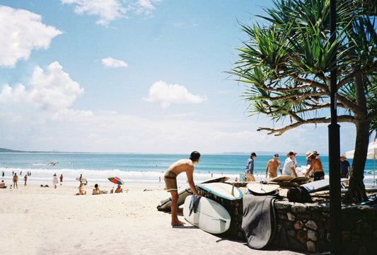 Noosa Main beach on a sunny day with a man in the foreground looking out to the ocean whilst putting away his surfboard