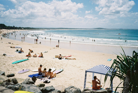 Noosa main beach with people sunbathing on the beach and others swimming in the ocean on a sunny and cloudy day