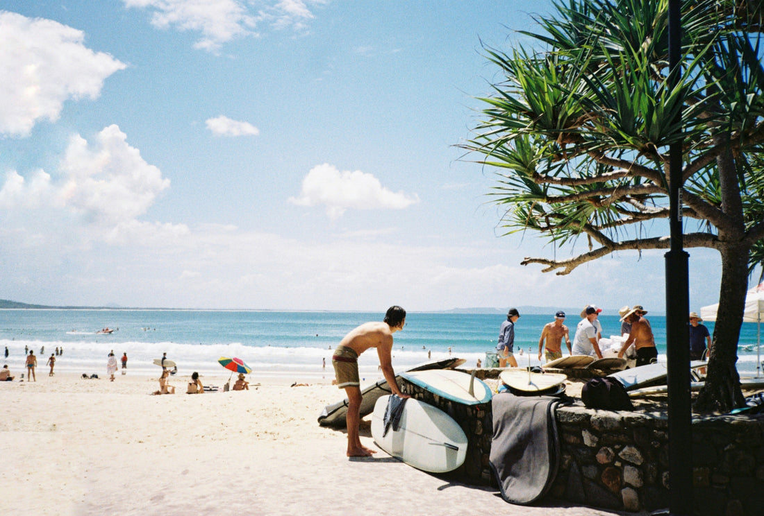 Noosa Main beach on a sunny day with a man in the foreground looking out to the ocean whilst putting away his surfboard