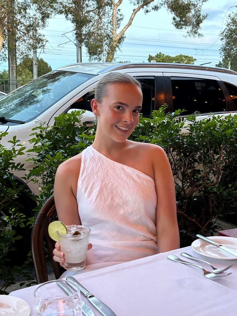 A girl out for dinner with a drink and a white dress on, looking very naturally tanned